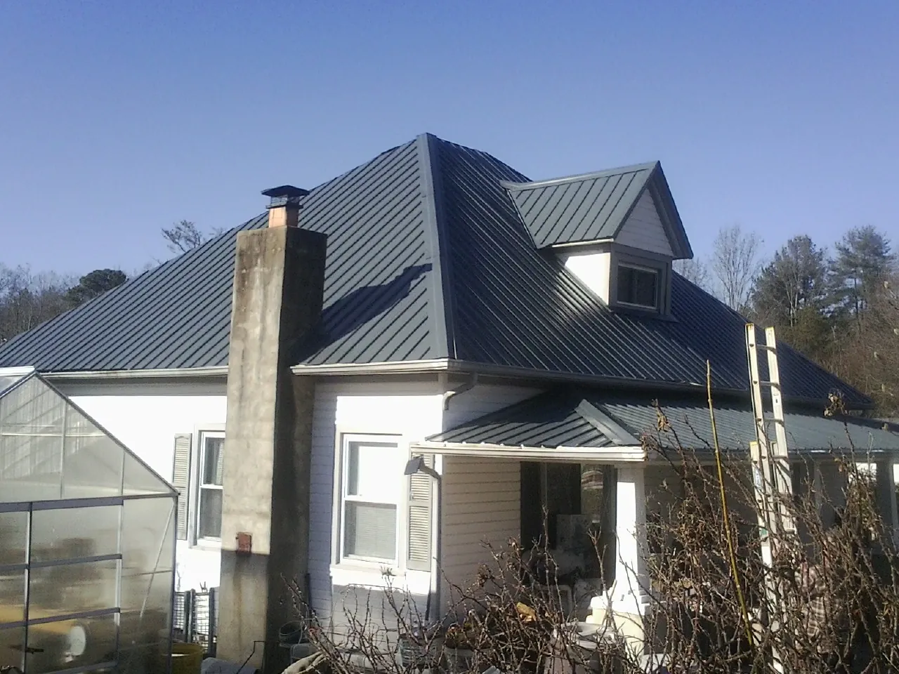 Dark blue standing seam metal roof on a white farmhouse with dormer — Slate & Tile Roof Repair by Roofing Brothers in Chauncey