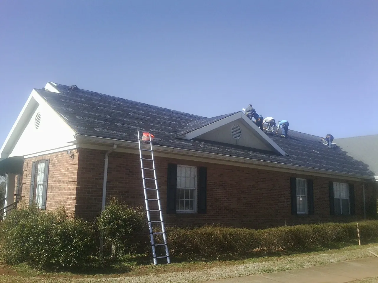 Crew tearing shingles off a brick ranch roof with a ladder set — Emergency Roof Repair work by our crew in Chauncey