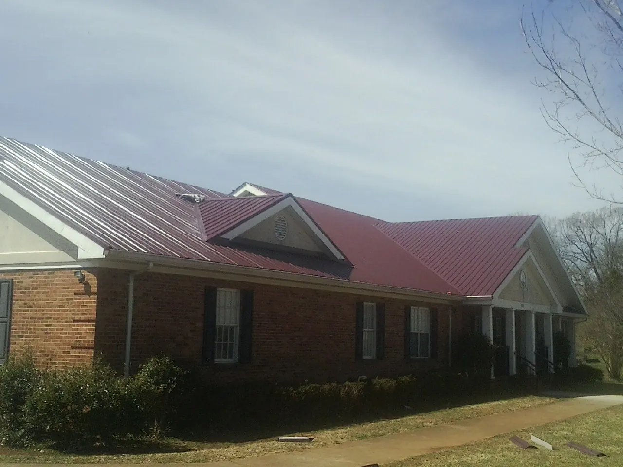Red metal roof with gabled entries on a long brick building, from a Hail Damage Roof Repair job in Chauncey