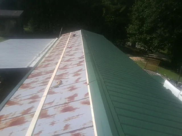 Old rusted panels beside newly installed green metal roofing — Wind Damage Roof Repair by Roofing Brothers in Chauncey