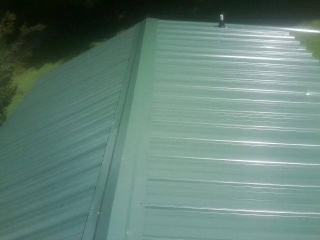 New green metal panels meeting at the ridge of a roof — Flat Roof Repair work by our crew in Chauncey