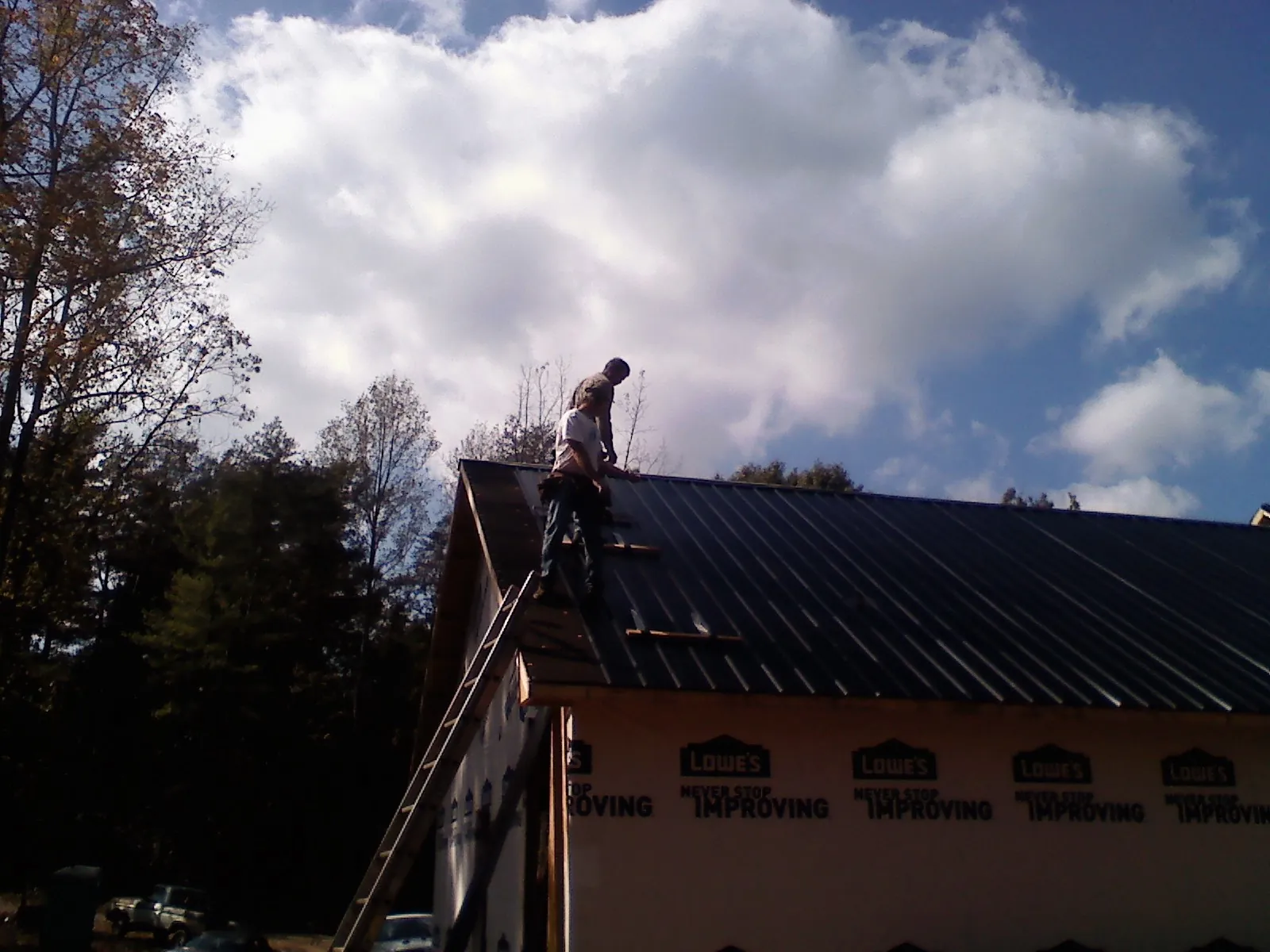 Roofer fastening dark metal panels high against a cloudy sky, from a Roof Inspection job in Chauncey