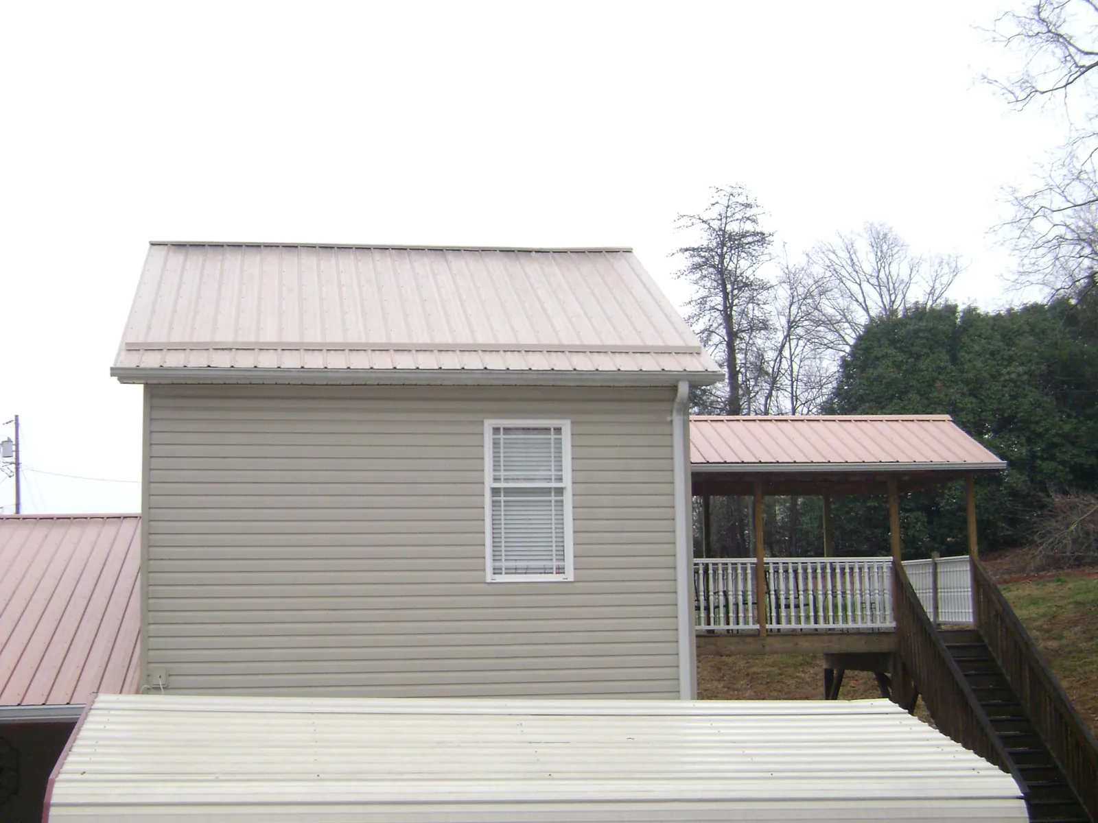 Tan metal roofs on a two story addition and attached porch, from a Roof Replacement job in Chauncey